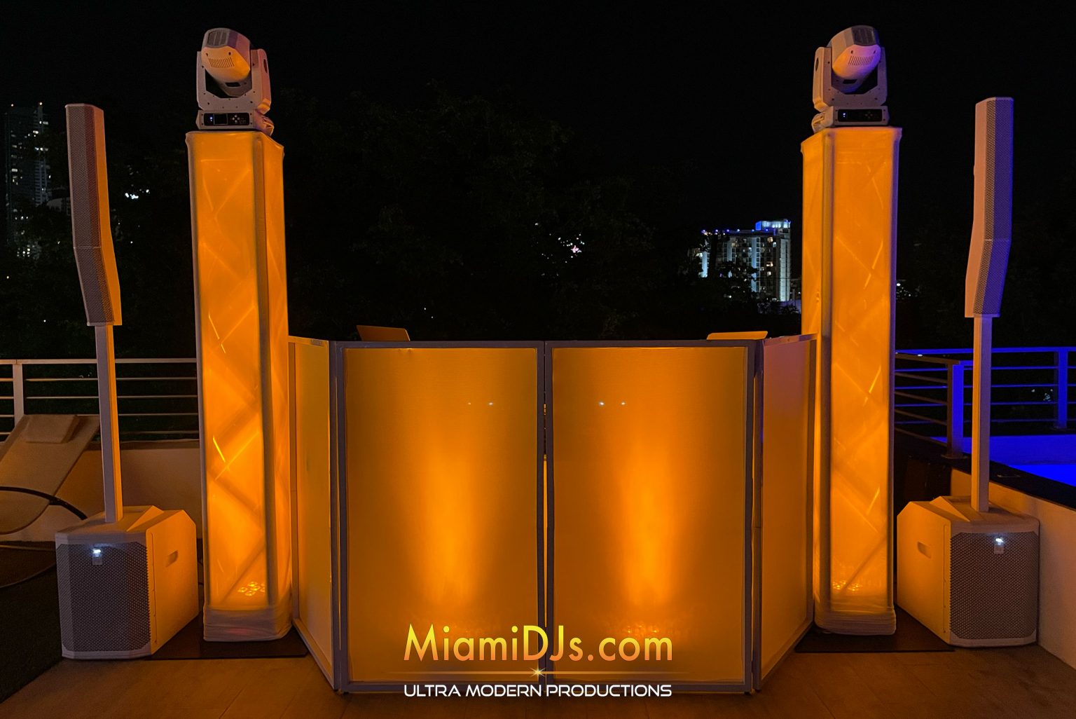 Select setup on a rooftop at night, white facade with two lit truss towers, LED moving heads and column array speakers
