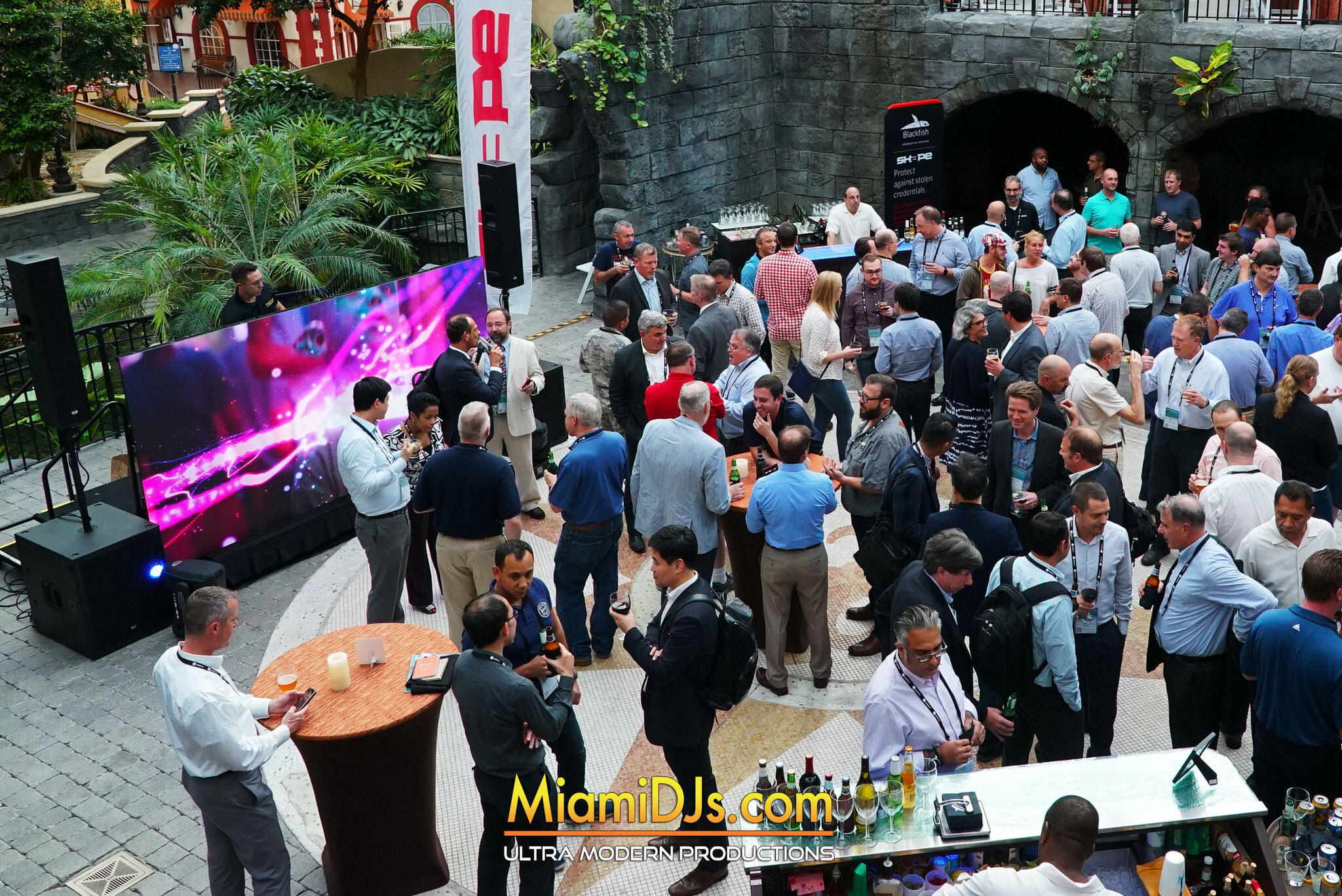 Several hundred badged guests at a corporate conference reception in front of a large LED wall