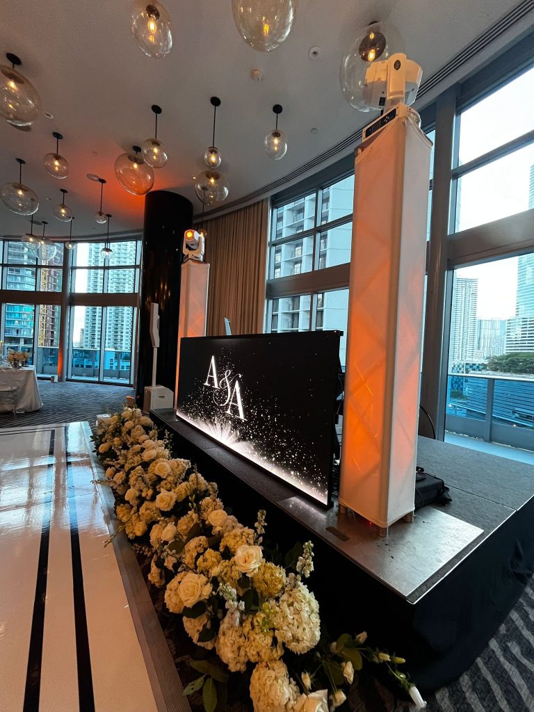 An A and A monogram on the LED booth above a wall of white and yellow florals