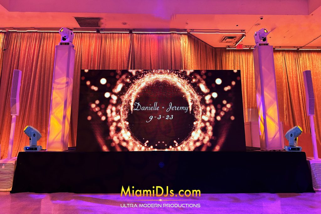 A ring of gold light around the couple's names on the LED wall, with amber draping behind