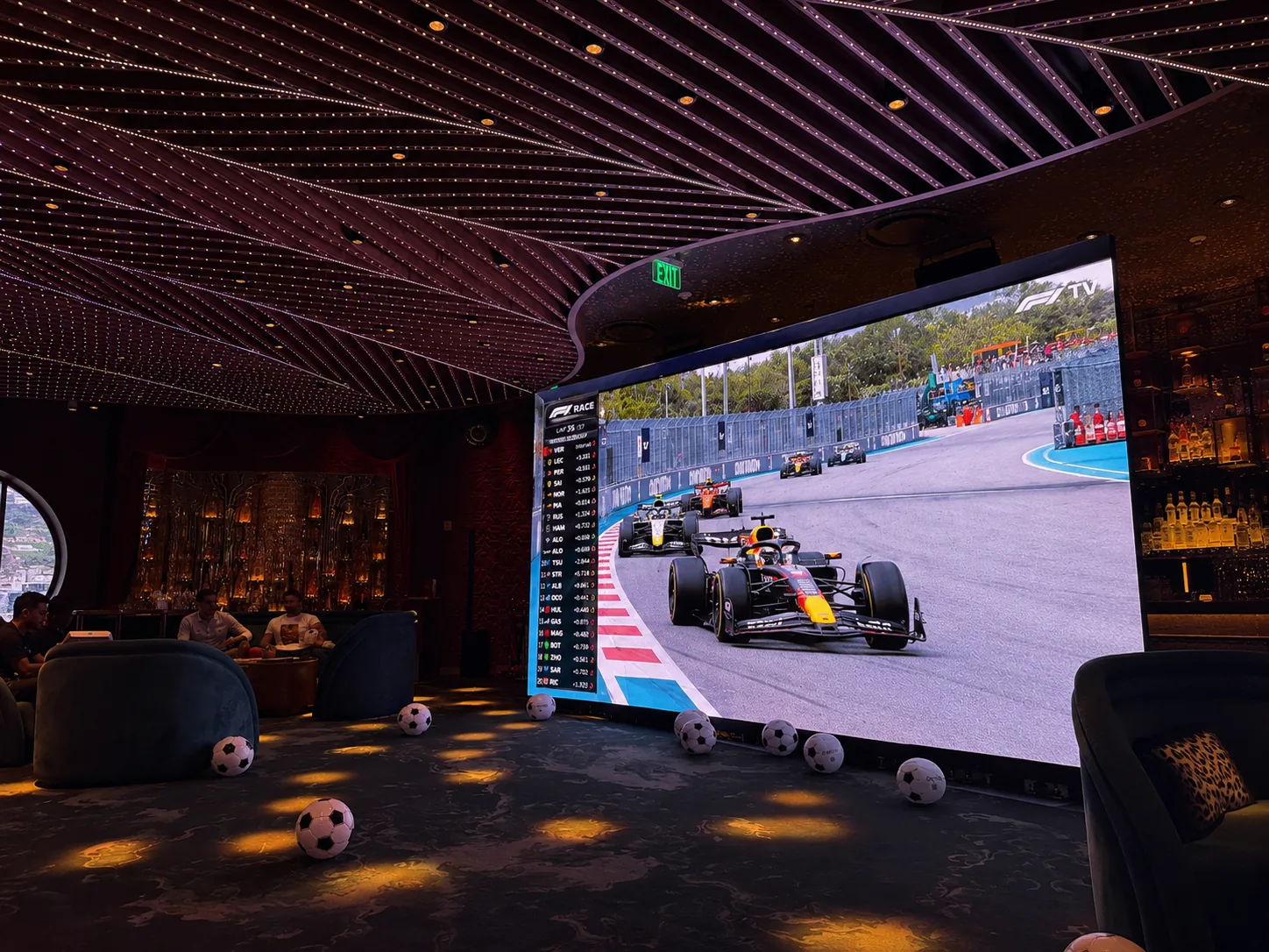 Miami DJs LED video wall showing the F1 Miami race at a lounge watch party under a lit ceiling